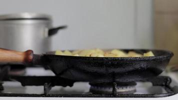 Braten frischer Kartoffeln in einer gusseisernen Pfanne mit Sonnenblumenöl. Blick auf einen Herd mit Bratpfanne gefüllt mit goldenen Bratkartoffeln in einer echten Küche. in einer hausgemachten Pfanne zubereitetes Essen. video