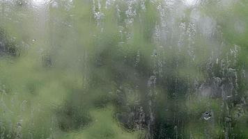 Lluvia Pesada. gotas de lluvia en el cristal de la ventana en un día de verano. enfoque selectivo, poca profundidad de campo. gotas de agua caen sobre una ventana mojada. vaso lleno de gotas durante un aguacero. panorama. video
