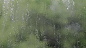 chuva pesada. gotas de chuva no vidro da janela em um dia de verão. foco seletivo, profundidade de campo rasa. gotas de água caem em uma janela molhada. copo cheio de gotas durante uma chuva. panorama. video