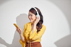 Happy cheerful Asian woman wearing wireless headphones listening to music from smartphone with lighting and shadow photo