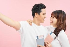 Portrait of successful lucky couple getting visa abroad holding raised fist showing passport with flying tickets shouting with wide open mouth isolated on pink background photo