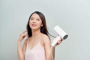 cuidado del cabello. hermosa mujer sonriente secando el cabello largo y recto saludable usando secador de pelo. foto