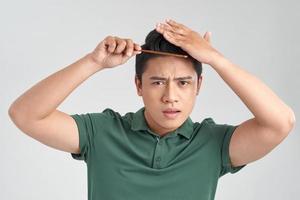 beauty, grooming and people concept - smiling young man brushing hair with comb over gray background photo