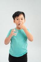 un niño con una camiseta blanca bebe una pastilla para la tos de un vaso transparente con agua foto