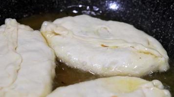 mujer chef prepara pasteles en aceite hirviendo. pasteles fritos con relleno. la anfitriona prepara patatas fritas o belyashi rellenas de verduras y carne, en una sartén en aceite. repostería casera, cocina. video