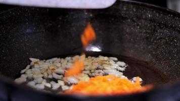 In a large pan with fried onions, the cook adds finely chopped carrots. Close-up of fried white onion. video