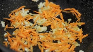 cebollas fritas y zanahorias en una sartén. zanahorias finamente picadas en una sartén grande con cebolla frita. primer plano de cebollas blancas asadas y zanahorias. video