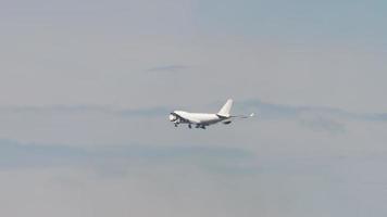 el avión de carga comercial blanco vuela en el cielo azul, baja el tren de aterrizaje y se prepara para aterrizar en el aeropuerto. luz del sol retroiluminada video