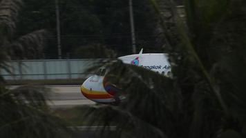 phuket, tailandia 26 de noviembre de 2019 - airbus de bangkok air acelerando antes de despegar en el aeropuerto de phuket, vista lateral a través de palmeras. video