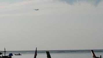 jet flygplan flygande på de horisont, nedåtgående till landa på de flygplats i phuket. båtar vingla på de Strand, de plan i de bakgrund. trafikflygplan över de hav video