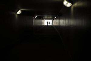 Two silhouettes at end of tunnel. Light in distance. Figures of small women in contrasting light. photo