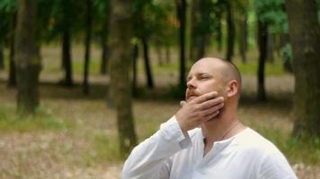 un homme en chemise blanche dans un parc avec une barbe réfléchit sur le sens de la vie video