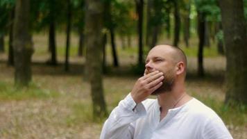A man in a white shirt in a park with a beard reflects on the meaning of life