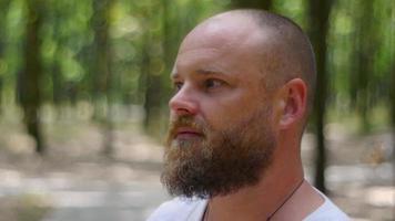 A man in a white shirt in a park with a beard reflects on the meaning of life video