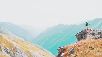 Statische Ansicht Solo-Wandererin steht auf einem Aussichtspunkt im Freien in den malerischen Bergen des Kaukasus. sorglose touristische frau, die sonne betrachtet, genießt landschaft. Wanderreisender auf dem Gipfel des Berges