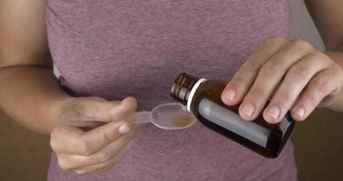 hand pour a bottle of medicinal syrup into a spoon
