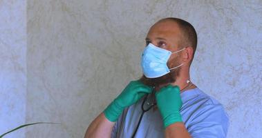 een Mens met een baard in een dokter pak zet Aan een masker video