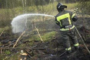 el bombero extingue el bosque. salvavidas vierte agua de la manguera. trabajo de servicio de rescate. foto