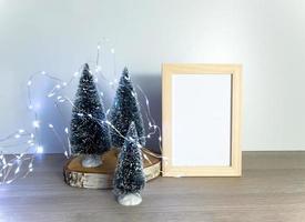 Christmas arrangement, little fir tree, blank photo frame, lights garland, festive composition with copy space for artwork presentation, mockup, winter holidays decor, selective focus