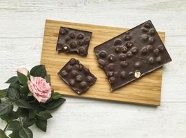 flat lay, broken chocolate bar on the wooden board and a pink rose photo