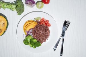 Vegan food red rice and vegetable broccoli tomato pumpkin on white background top view. photo