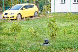 An automatic sprayer waters a young garden and lawn in the backyard of a residential building. photo