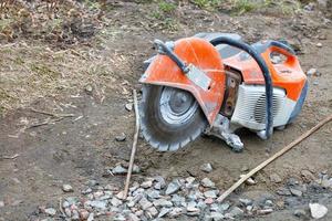 Manual petrol cutter with a diamond wheel on a blurred background of crushed stone and sandy soil. photo