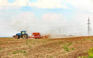 un tractor agrícola con una sembradora remolcada cultiva la tierra en el campo aplicando los fertilizantes necesarios. foto