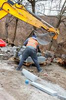 A construction worker using an excavator boom and bucket unloads concrete curbs at a work site. photo