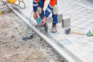 A construction worker evenly cuts paving slabs with a grinder when paving a sidewalk. photo
