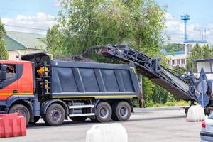 A road miller removes the top layer of old asphalt from a road section and loads it onto a dump truck. photo