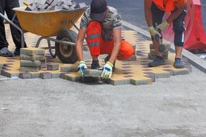 Builders laying colorful paving stones in a geometric pattern on a sunny day. photo