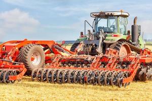 un potente tractor agrícola combinado con una grada de discos roja de varias hileras en un día de verano. foto