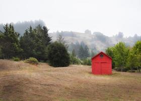 pequeño granero rojo en el campo con colinas neblinosas foto