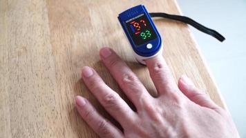 Asian man hands using modern fingertip blood oxygen meter on wooden table,closeup video