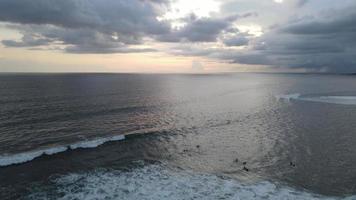 Aerial view of people surfing on waves during sunset when vacation in Bali, Indonesia.