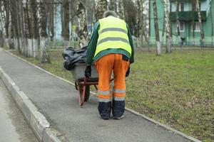 Worker carries cart of garbage. Work clothes of bright color. Cart with bags. photo