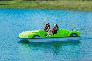 Girls in safety jackets wave and ride a pedal boat on a mountain lake photo