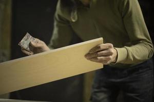 Carpenter grinds board. Man creates furniture. Hands hold sanding paper. photo
