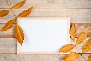 Hello autumn concept. Empty frame mock up on wooden background and yellow fallen leaves. photo