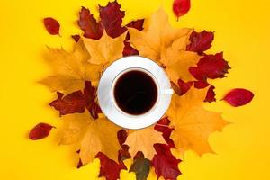 Cup of coffee and fallen leaves on bright yellow background. Hello autumn concept. Hot drink for cold weather. photo