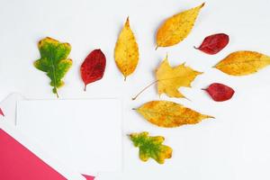 Autumn flat lay. Envelope with a blank greeting card and fallen yellow leaves on white background. photo