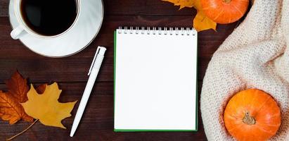 Autumn morning concept. Cup of hot espresso coffee and fallen leaves on wooden background. Mockup notebook, knitted sweater and pumpkins. photo