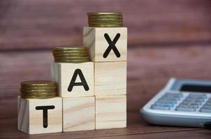 Tax word on wooden blocks with gold coins on top and calculator background. Tax concept photo