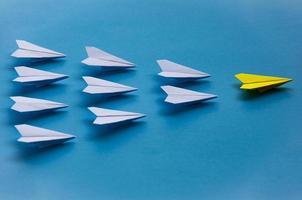 Yellow paper plane origami leading white planes on blue background. Leadership skills concept photo