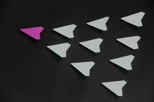 Purple paper plane origami leading white planes on dark background. Leadership skills concept photo