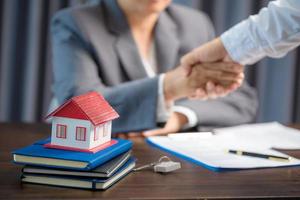 Woman home sales person is checking documents for house purchase contract before letting the customer sign contract on table is key with house model, real estate trading and insurance property concept photo