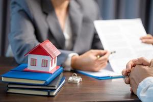 Woman home sales person is checking documents for house purchase contract before letting the customer sign contract on table is key with house model, real estate trading and insurance property concept photo