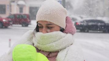 una mujer abraza a un pequeño perro blanco afuera en la nieve, ambos con abrigos hinchados video