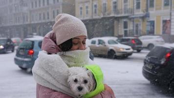 femme câlins petit chien blanc à l'extérieur dans la neige à la fois portant des manteaux gonflés video